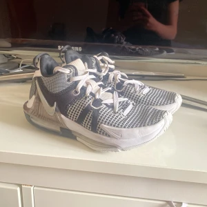 Nike Lebron Witness 7 svart/vit  - Säljer ett par svart/vita basketskor med rutigt meshmönster och vita detaljer. Skorna har snörning, rund tå och en sportig design med tydlig Nike-logga på sidan och mönstrad häl. Basketskor. Använda. 