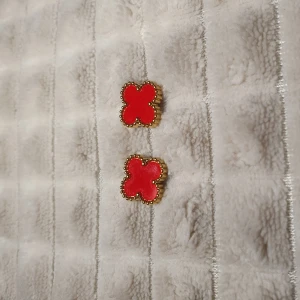 Röda fyrklöverformade örhängen - Snygga röda örhängen i form av fyrklöver med en fin guldfärgad kant. Perfekta för att ge en färgklick till din outfit. Passar både till vardag och fest.