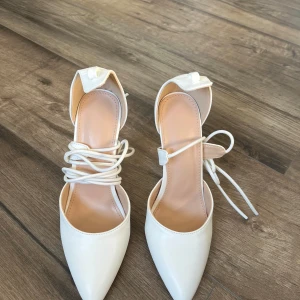 Vita klackskor med snörning och spetsig tå - Säljer ett par vita klackskor med spetsig tå och smal klack. Skorna har långa snören som kan lindas runt vristen och en elegant design. Perfekta för dig som vill ha en stilren och trendig look. Köpta från SHEIN för 260kr 