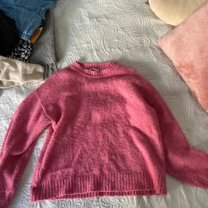 Rosa stickad tröja - Mysig rosa stickad tröja med rund halsringning och långa ärmar. Tröjan har ribbade muddar vid ärmslut och nederkant, perfekt för lager på lager under kyliga dagar.