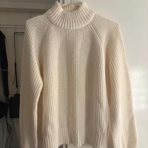 Vit stickad polotröja från Noisy May - Krämvit stickad polotröja från Noisy May. Tröjan har en hög ribbad krage, lång ärm och breda ribbade muddar vid ärmslut och nederkant.