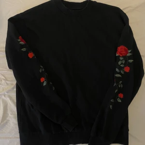 Svart sweatshirt NA-KD - Svart sweatshirt från NA-KD med detaljer (rosor) på båda ärmarna. Sparsamt använd, pris går alltid att diskutera!