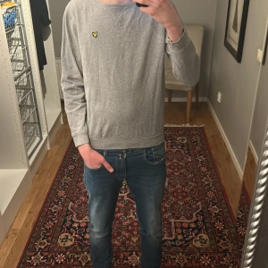 Grå sweatshirt från Lyle & Scott - Säljer en stilren grå sweatshirt från Lyle & Scott Junior med den klassiska gula loggan broderad på bröstet. Tröjan har rund hals och långa ärmar, perfekt för en avslappnad look.priset står inte skrivet i sten!!!
