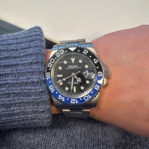 Seiko GMT Master ”batman” lookalike  - Knappt använd, kostar nypris 4500kr på timecraft.se box och tillbehör samt extra länkar tillkommer. Detta är en Seiko automatisk klocka med rostfritt stålarmband, svart urtavla och blå/svart vridbar bezel. Klockan har tydliga index, datumvisning och safirglas. Baksidan har genomskinligt fönster som visar urverket. 