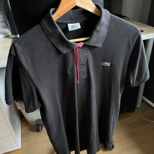 Svart pikétröja från Lacoste - Säljer en svart pikétröja från Lacoste i storlek L, men den passar bättre som en M. I fint skick. 