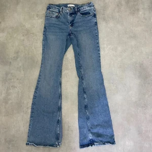 Blå bootcut jeans - Säljer ett par klassiska blå bootcut jeans med råa kanter nertill. Jeansen har fem fickor och stängs med dragkedja och knapp. Perfekta för en avslappnad och trendig look.
