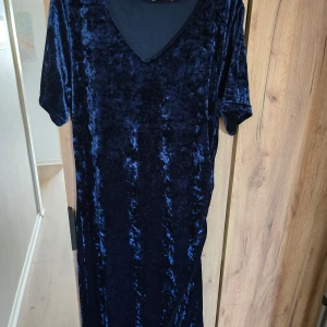 Mörkblå sammetklänning med v-ringning - Säljer en lång mörkblå klänning i mjuk sammet med v-ringad hals och korta ärmar. Perfekt för dig som vill ha en elegant och bekväm look. Klänningen har en rak passform och känns lyxig tack vare materialet.