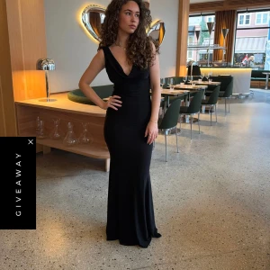 Svart långklänning med öppen rygg - Säljer en elegant svart långklänning med djup v-ringning och öppen rygg. Klänningen har en figurnära passform och är perfekt för festliga tillfällen. Tidlös och stilren design som framhäver siluetten.