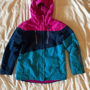 Färgglad vinterjacka från Campri - Säljer en färgstark vinterjacka från Campri i blått, turkost och cerise med huva. Jackan har dragkedja framtill, flera fickor med dragkedja och justerbara ärmslut. Perfekt för kalla dagar och vintersport.