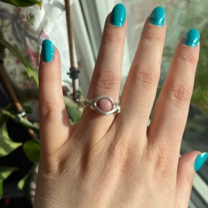 Silverring med rosa sten - Unik silverring med en rund, rosa sten i mitten. Ringen har en elegant och handgjord känsla med detaljerade sidor. Perfekt för dig som vill ha ett smycke som sticker ut och ger en personlig touch till din stil.