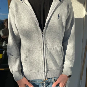 Grå hoodie från Polo Ralph Lauren - Säljer en klassisk grå hoodie från Polo Ralph Lauren i storlek XS. Tröjan har dragkedja, två fickor fram och broderad logga på bröstet. Mjuk insida och fodrad huva i mörkblått. Perfekt för en avslappnad stil. Bara att skriva vid minsta fråga, pris kan diskuteras.