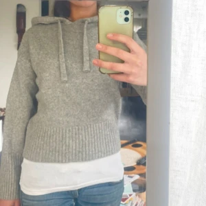 Grå stickad hoodie från Zara - Mysig grå stickad hoodie från Zara med huva och dragsko. Tröjan har långa ärmar och bred ribbad mudd vid ärmslut och nederkant. Perfekt för en avslappnad och stilren look.