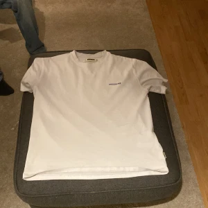 Vit t-shirt från Woodbird med tryck - Vit t-shirt från Woodbird i bomull med blått tryck fram och stort grafiskt tryck på ryggen. Klassisk passform och rund hals. Perfekt för en avslappnad stil. Ny pris 599kr 