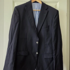 Mörkblå kavaj - Klassisk mörkblå kavaj i 100% ull med två knappar framtill och fickor med lock.