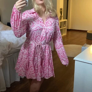 Rosa och vit mönstrad skjortklänning - Säljer en söt rosa och vit skjortklänning med knyt i midjan och långa ärmar. 