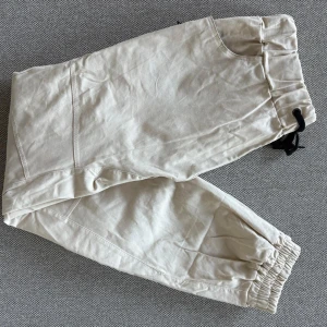 Beiga byxor - Säljer ett par beiga med elastisk midja och svart snörning. Byxorna har fickor på sidorna och baktill samt elastiska vid bensluten. Perfekta för en avslappnad stil.