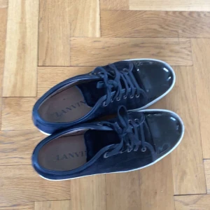 Svarta sneakers från Lanvin med lackad tå - Säljer ett par svarta sneakers från Lanvin med snygg lackad tå och vita sulor. Skorna har snörning och en klassisk rund tå. Perfekta för dig som vill ha en stilren och exklusiv look.