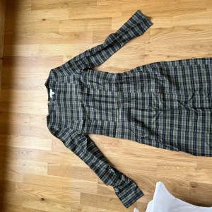 Rutig långärmad klänning från H&M - Snygg långärmad klänning från H&M i rutigt mönster med dragkedja i sidan. Klänningen har en figurnära passform och går i mörka toner av blått och grått. Perfekt för dig som gillar klassiska mönster med modern twist.