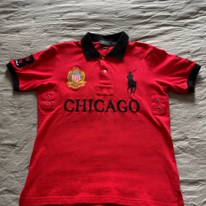Röd piké t-shirt från Polo Ralph Lauren - Säljer en röd piké t-shirt från Polo Ralph Lauren med svart krage och detaljer. Stor broderad logga och texten 'CHICAGO' framtill, samt nummer 3 på ryggen. Broderad emblem på bröstet och svarta detaljer på ärmarna. Pris kan diskuteras 