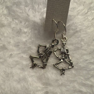 Silverfärgade skelettörhängen - Unika örhängen i form av dansande skelett i silverfärg. Perfekta för dig som vill sticka ut med ett coolt och annorlunda smycke. Passar extra bra till temafester eller halloween. Krokarna är i sterling silver