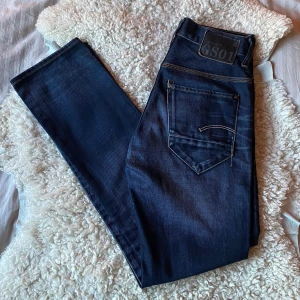 Mörkblå jeansbyxor från G-Star RAW GS01 - Säljer ett par sjukt schyssta mörkblå jeansbyxor från G-Star RAW, modell GS01. Jeansen har klassisk femficksdesign, slim passform och snygga kontrastsömmar. Märkespatch bak i midjan och diskreta slitningar framtill för en cool look. Jeansen passar i alla årstider och befinner sig i skicket 9.5/10. Tveka inte på att höra av dig vid frågor eller funderingar! ⭐️