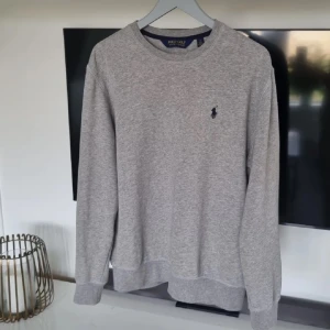 Grå sweatshirt från Polo Golf Ralph Lauren - Klassisk grå sweatshirt från Polo Golf Ralph Lauren med rund halsringning och broderad logga på bröstet. Mjuk bomullskänsla och ribbade muddar vid ärmslut och nederkant. Bra skick. Deras golf kollektion, väldigt skön och bra kvalite. Har QR kod, alltså äkta.