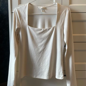 Vit långärmad topp med fyrkantig ringning - Säljer en stilren vit långärmad topp med fyrkantig ringning. Perfekt att matcha med jeans eller kjol för en clean look. Snygg basic som passar till mycket!