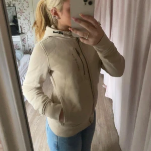 Beige hoodiejacka från Sail Racing - Säljer en beige hoodiejacka från Sail Racing med dragkedja framtill och huva. Jackan har långa ärmar, fickor och en sportig look. Perfekt för vår och höst. Snygg och enkel att matcha till jeans eller leggings. Knappt andvänd och köptes i december månad sedan för cirka 1500💗