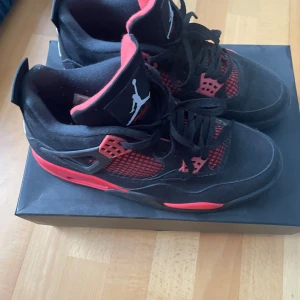 Svarta och röda Nike Air Jordans - Säljer ett par Nike Air Jordans i svart och rött med klassisk Jumpman-logga på plösen och hälen. Skorna har snörning, meshpaneler på sidorna och platt sula. Perfekta för dig som gillar streetwear och vill sticka ut med snygga detaljer.