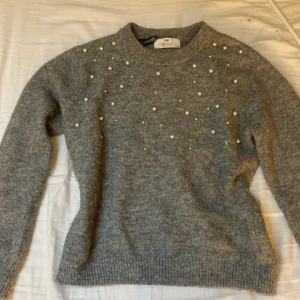 Grå stickad tröja med pärlor från H&M - Superfin grå stickad tröja från H&M med pärldetaljer framtill. Tröjan har rund halsringning och långa ärmar. 🩷