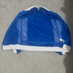 Blå och vit träningsjacka Espanyol de Barcelona Academy - Säljer en blå och vit träningsjacka med dragkedja från Espanyol de Barcelona Academy. Jackan har klubbens logga på bröstet och text på ryggen. Perfekt för fotbollsträning eller som sportig vardagsstil.