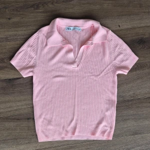 Rosa ribbad pikétröja från Zara - Säljer en ljusrosa ribbad pikétröja från Zara med korta ärmar och klassisk krage. Tröjan har en mjuk och stretchig känsla, perfekt för en avslappnad men ändå stilren look. Aldrig använd. Passar även nån med storlek s.