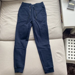 Mörkblå mjukisbyxor från Peak Performance - Mörkblå mjukisbyxor från Peak Performance med resår och snörning i midjan samt muddar vid bensluten. Byxorna har två sidofickor och är tillverkade i mjukt material, perfekta för en avslappnad stil. (För små för mig)