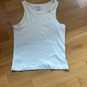 Vit ribbad linnetopp från Lindex - Säljer en klassisk vit ribbad linnetopp från Lindex i storlek 158/164. Toppen är ärmlös och har rund halsringning. Perfekt för varma dagar eller som lager under andra plagg. Linnet är rätt så kort och är lite över naveln på mig som är 164💕
