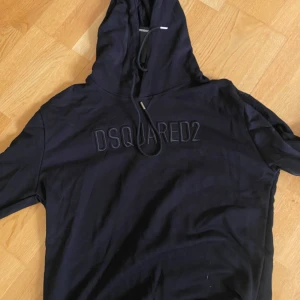 Svart hoodie från Dsquared2 - Svart hoodie från Dsquared2 med broderad logga på bröstet och justerbar huva med snörning. Perfekt för en avslappnad och stilren look. Passar S/M/L