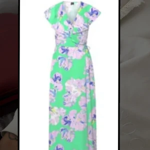 Grön blommig långklänning - Säljer en långklänning i grönt med stora blommiga mönster i lila, blått och vitt. Klänningen har en luftig passform. Omlott snörning. Från Vera Moda. Använd en kväll 