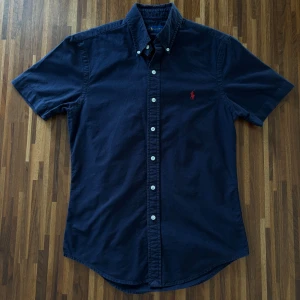 Mörkblå kortärmad skjorta från Ralph Lauren - Mörkblå Ralph Lauren skjorta   |  Skick 8/10 |  Size S |  Slim fit  |  Bredd 44,5 cm Längd 70 cm  |  Perfekt för en stilren look till sommaren.  Hör av dig vid minsta fråga eller fundering :)