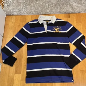 Randig rugbytröja från Ralph Lauren - Tjena, Säljer en snygg långärmad piké  från Ralph Lauren i blått, svart och vitt med broderad logga på bröstet. Tröjan är aldrig andvänd då den är för stor så mycket bra skick. Priset kan diskuteras🙌🤝