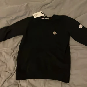 Svart Moncler tröja/sweatshirt - Säljer en svart sweatshirt från Moncler med rund halsringning och Moncler-logga på bröstet. Tröjan har långa ärmar och klassisk passform. Perfekt för dig som gillar stilrena märkesplagg. NFC finns kom dm för mer info