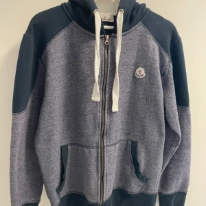 Grå moncler cardigan - Säljer en sparsamt använd grå hoodie från Moncler med svarta detaljer och vit dragsko. Jackan har dragkedja framtill, fickor och Moncler-logga på bröstet. Perfekt för en avslappnad stil. Skick 8/10 Nypris 7299 mitt pris 1400 Passar 170-180 cm