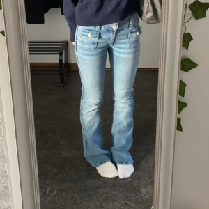 Ljusblå bootcut jeans från hm - Säljer ett par ljusblå jeans med bootcut passform och två stora fickor framtill med silverfärgade knappar. Jeansen har normal midja och klassisk femficksdesign. Perfekta för en avslappnad och trendig look. Storlek 158, men passar mig som vanligtvis har xs/s, och de är väldigt stretchiga.