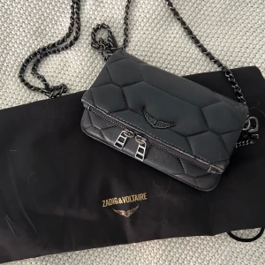 Svart quiltad axelväska från Zadig & Voltaire - Snygg svart quiltad axelväska från Zadig & Voltaire med kedjerem och silverfärgade detaljer. Väskan har dubbla dragkedjor framtill. Den är liten💖