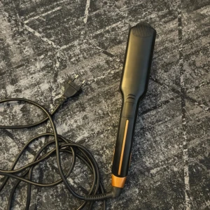 Svart och guldig plattång - Säljer en svart plattång med guldiga keramiska plattor och digitala knappar på handtaget. Perfekt för att styla håret rakt eller skapa mjuka vågor. Lång sladd med EU-kontakt för smidig användning.