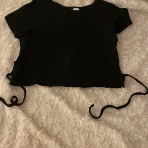 Svart croppad topp med knytband - Svart croppad topp med korta ärmar och lite öppen i ryggen men knyte. Mjuk och stretchig känsla i materialet.