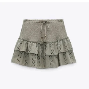 Grön volangkjol med broderade detaljer - Supersöt grön kjol med smock i midjan och knytband med tofsar. Kjolen har två lager volanger och fina broderade hålmönster. Perfekt för dig som gillar en feminin och trendig stil.