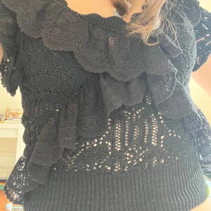 Svart spetsblus med volang - Säljer en svart blus med vackra spetsdetaljer och stora volanger längs ringningen. Blusen är ärmlös och har ett feminint, romantiskt uttryck. Perfekt att styla med jeans eller kjol. Aldrig använt!!!💗💗