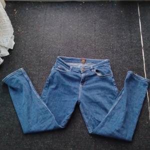 Blå jeansbyxor från Lee - Säljer ett par klassiska blå jeansbyxor från Lee med raka ben och normal passform. Byxorna har fem fickor, dragkedja och knapp med Lee-logga framtill. Perfekta för dig som gillar tidlös denimstil. 
