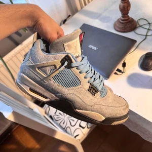 Jordan 4 Retro University Blue - Säljer ett par Jordan 4 Retro University Blue med ovandel i ljusblå mocka, svarta och grå detaljer samt meshpaneler på sidorna. Skorna har klassisk snörning, platt sula och Jumpman-logga under sulan.