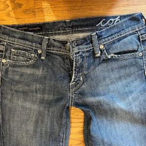 Mörkblå bootcut jeans från 7 For All Mankind - Säljer ett par mörkblå jeans från 7 For All Mankind med bootcut passform. Jeansen har klassiska fem fickor, snygga slitningar och kontrastsömmar. Bakfickorna har broderad detalj. Perfekta för dig som gillar en tidlös jeansstil.