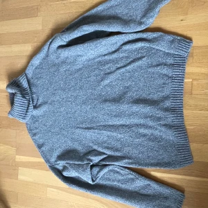 Grå stickad polotröja från NA-KD - Mysig grå stickad polotröja från NA-KD. Tröjan har lång ärm, ribbade muddar och hög polokrage. Perfekt för kyligare dagar och enkel att matcha med olika outfits.